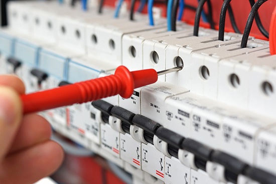 Hand of electrician with multimeter probe at electrical switchgear cabinet